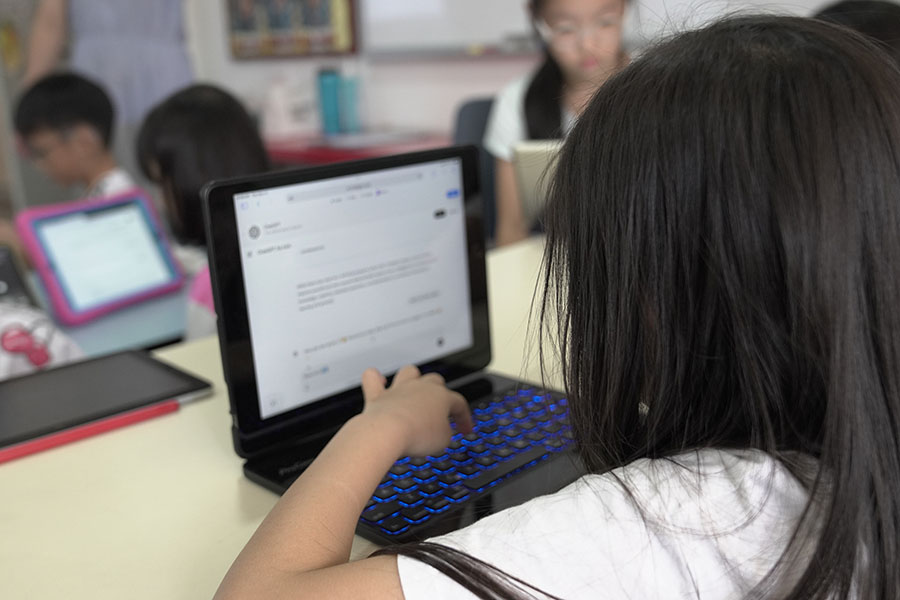 Child uses laptop in classroom, typing on keyboard with blue backlight