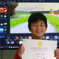 Young boy holds certificate in front of video editing screen