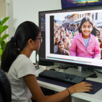 Young woman edits photo of smiling girl in pink jacket on computer screen