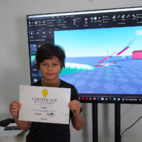 Boy holds certificate in front of large screen displaying 3D modeling software