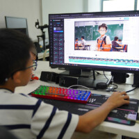 Young boy edits video on computer with colorful keyboard and monitor