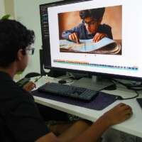 Young person edits photo of child reading on computer screen