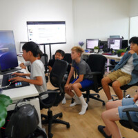 Children and adults gather around computers in a tech workshop