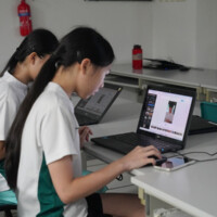 Two students work on laptops at a classroom desk