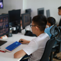 Young man works at computer station in tech lab with others nearby