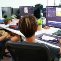 Two people work at desks with multiple monitors and editing software