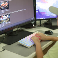 Young gamer focuses on video editing on dual monitors with glowing keyboard
