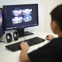 Child uses computer, viewing colorful graphics and a nature scene on dual monitors