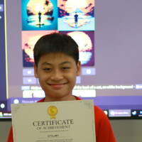 Smiling boy holds certificate of achievement in front of computer screen