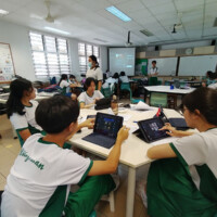 Students use tablets in a modern classroom with teacher and screens