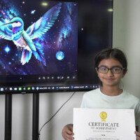 Girl holds certificate in front of large screen displaying colorful hummingbird