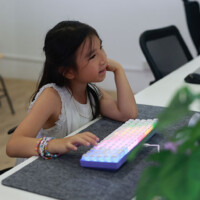 Young girl focused on computer with colorful keyboard, thoughtful expression