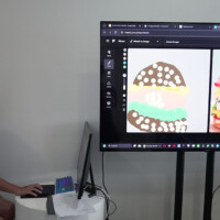 Child uses laptop, viewing burger images on large screen