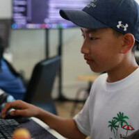 Young boy focused on computer, wearing cap and t-shirt