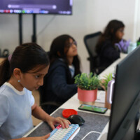 Young girl focused on computer, others working in background