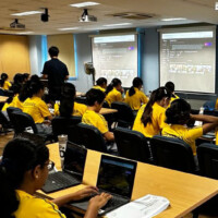 Students in yellow shirts use laptops in a classroom with projectors
