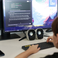 Person coding on computer with dual monitors and speakers