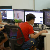Two young men work at desks with multiple computer monitors