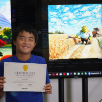 Young boy holds certificate, smiling behind large screen displaying animated scene