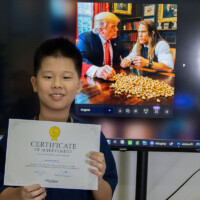 Young boy holds certificate, smiling in front of screen displaying Trump and woman