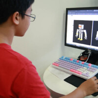 Young boy in red shirt designs robot characters on computer screen