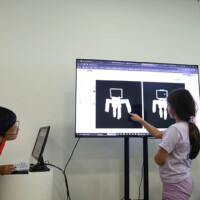 Two children interact with a large screen displaying robotic figures