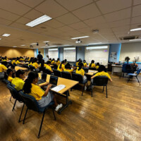 Students in yellow shirts sit at desks in a classroom