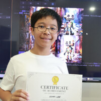 Young boy holds certificate, smiling in front of computer screen