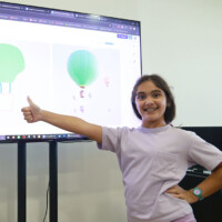 Smiling girl gives thumbs-up in front of digital hot air balloon display
