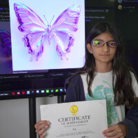 Girl holds certificate, stands beside screen displaying purple butterfly