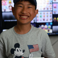 Smiling boy holds certificate, wears Mickey Mouse shirt with American flag