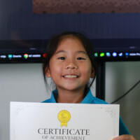 Smiling girl holds certificate of achievement in front of computer screen