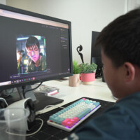 Young person edits video on computer with colorful keyboard and headphones