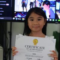 Young girl holds certificate of achievement in front of monitors