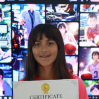 Young girl holds certificate in front of large screen displaying various images