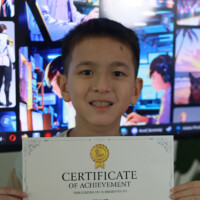 Young boy smiles while holding certificate in front of gaming screens