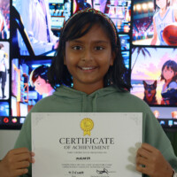 Smiling girl holds achievement certificate in front of large screen displays