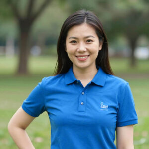 Smiling woman in blue polo shirt stands outdoors in park setting