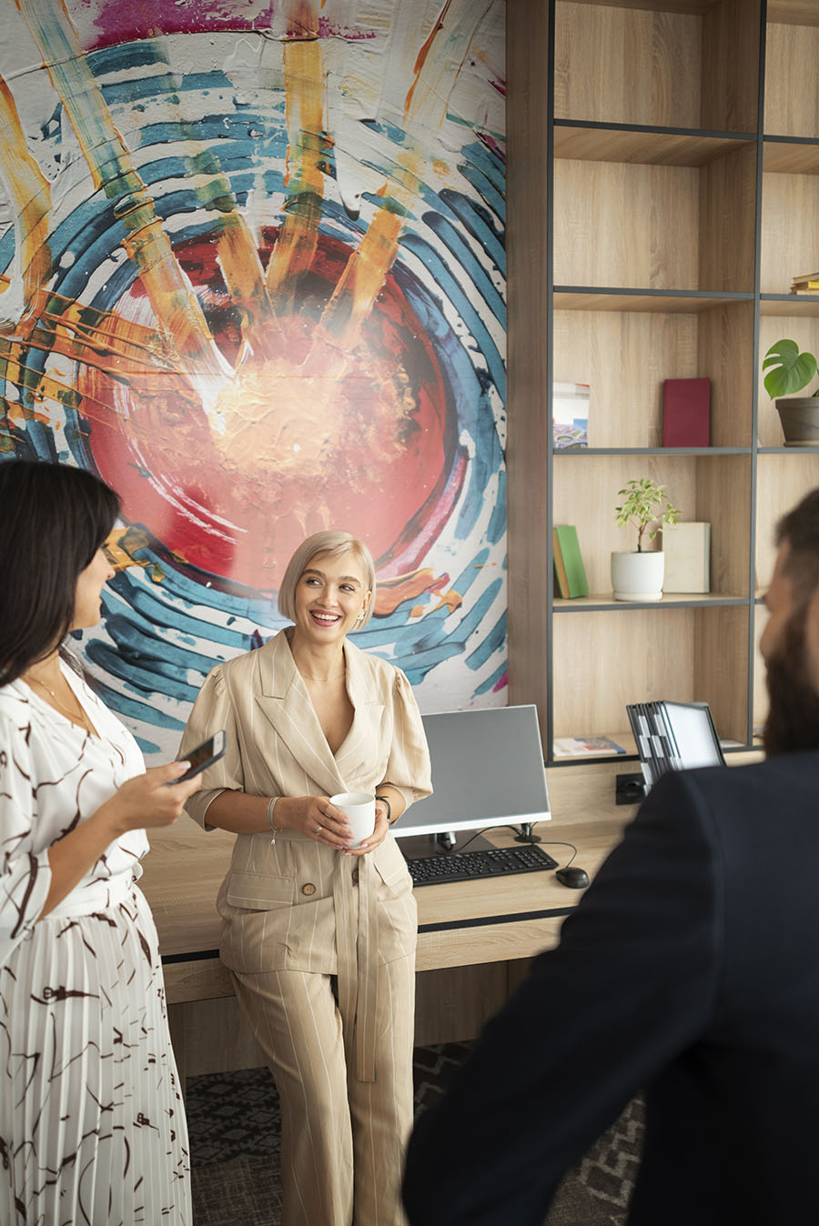 Three people in modern office, one holding coffee, smiling